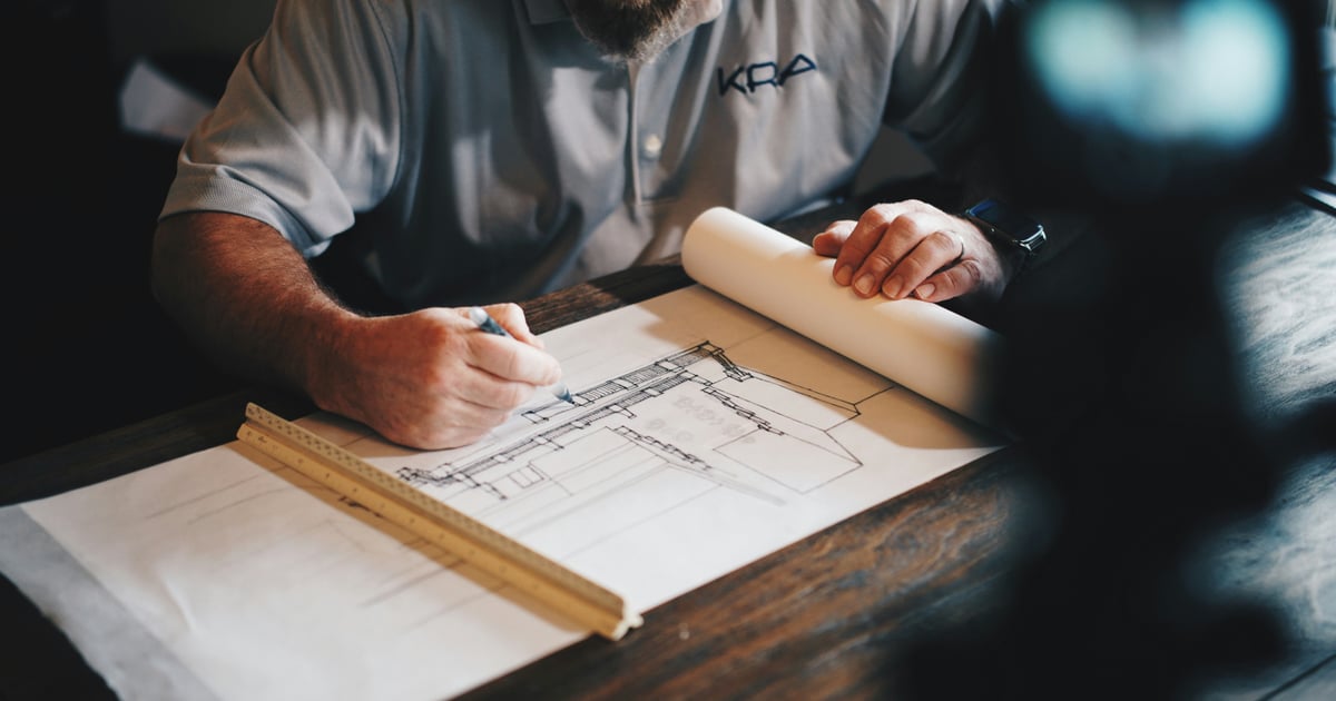 A tradesperson's hands sketching on an architectural blueprint with a ruler.