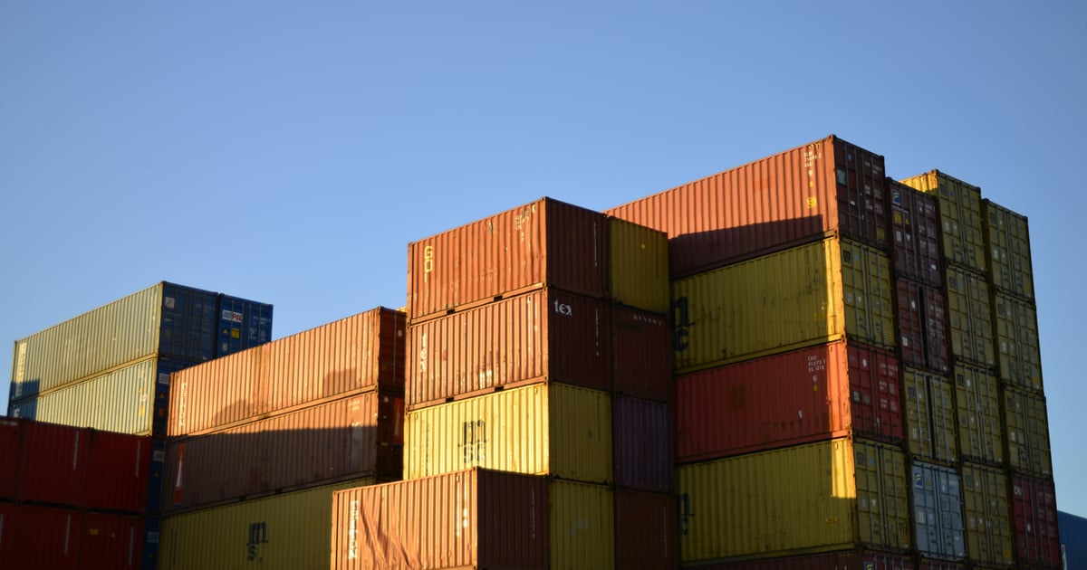 Stacks of weathered shipping containers in orange, yellow and red under a clear blue sky.