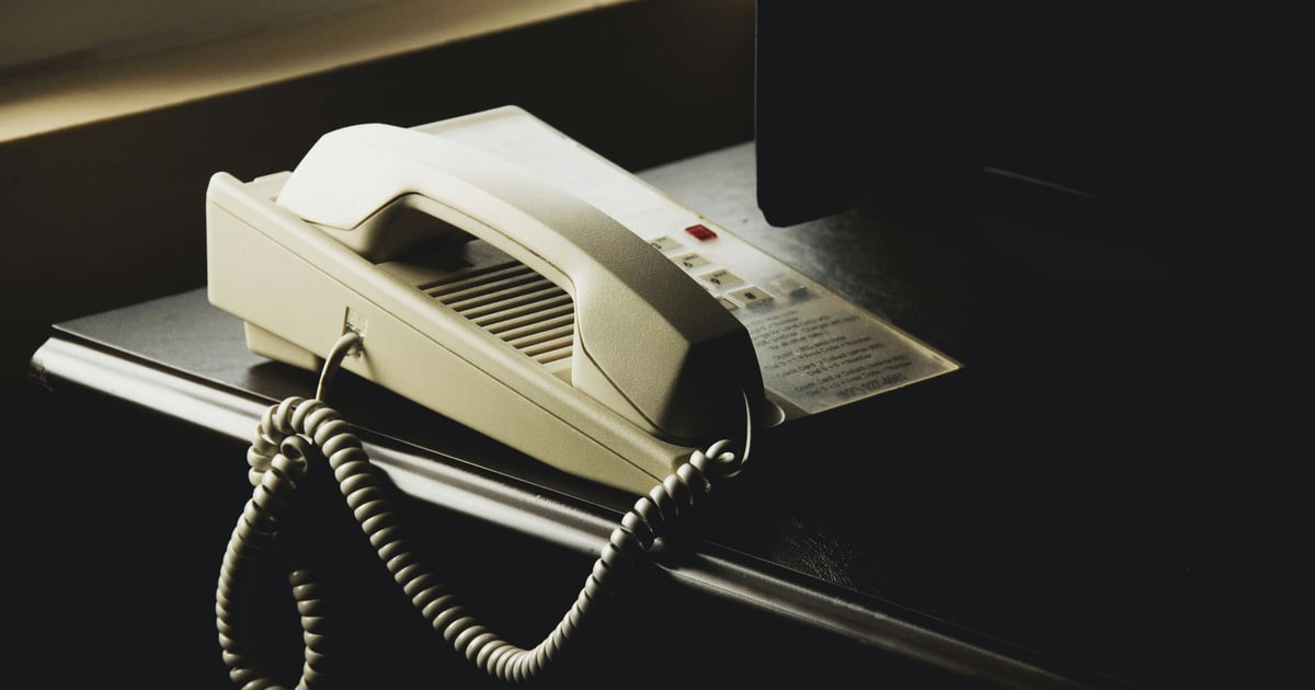 An old cream-colored landline desk phone on a dark desk, moodily lit.