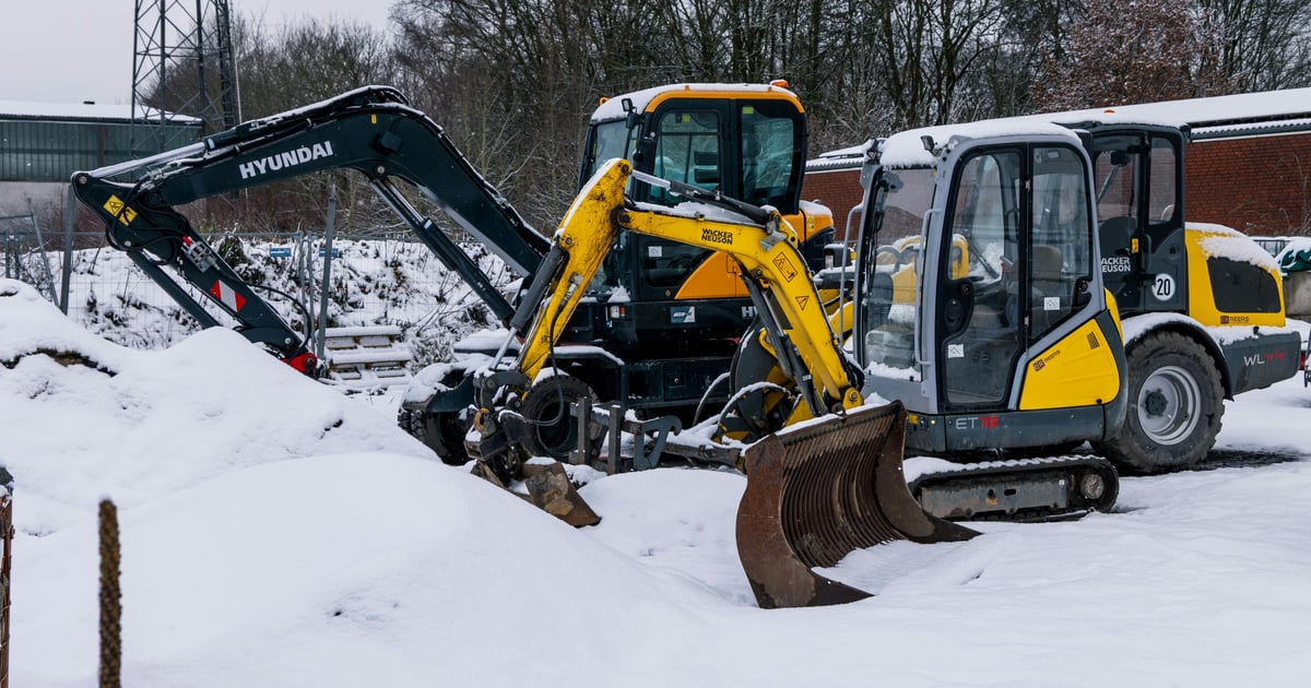 Yellow excavator and compact loader parked on a snow-covered job site in winter.